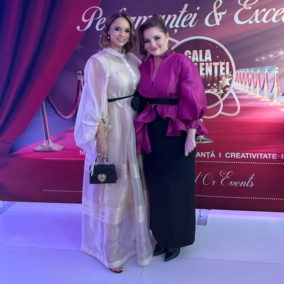 Two people posing on a clean white floor in front of a red and violet backdrop adorned with text and decorative elements, capturing the essence of the Gala of Excellence and Performance 2024 in Romania.